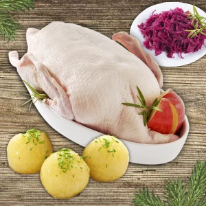 Weihnachtsgans Komplettpaket: Weihnachtsgans in weißer Schale mit Kartoffelknödeln und Rotkraut auf hellem Holzhintergrund